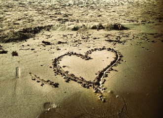 Symbol of summer love a romantic heart shape drawn on the sand of a sunny beach coast, washed by the ocean water wave