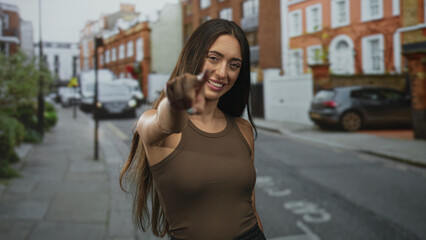 Young hispanic woman smiling and raising fists with bare arms on a city street in sleeveless top; personal success triumph.
