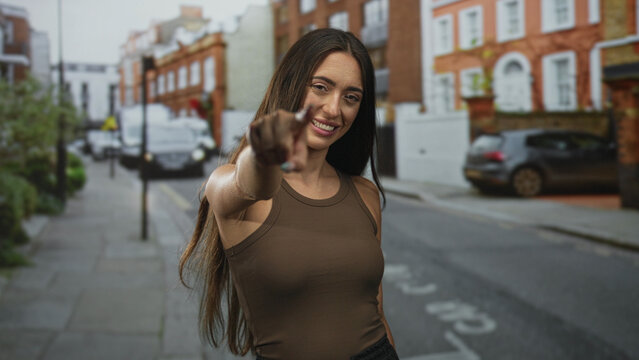 Young hispanic woman smiling and raising fists with bare arms on a city street in sleeveless top; personal success triumph. - Powered by Adobe
