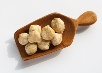 Candlenuts (Kemiri) on a brown wooden scoop, isolated on a white background.