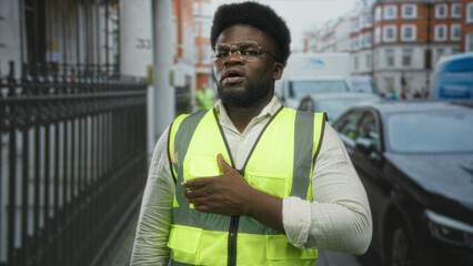 Man in neon yellow high visibility vest gesturing with hand to chest amid traffic and parked cars...
