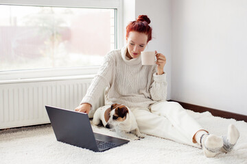 Smiling Young Woman Sitting on carpet and using Laptop by dog at Home