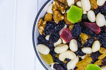 Various varieties of raisins, assorted nuts in a bowl on a white wooden background. View from above
