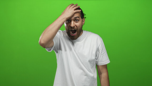 Young arab hispanic man in white t shirt with hand on forehead and open mouth in green screen studio; surprise realization. - Powered by Adobe