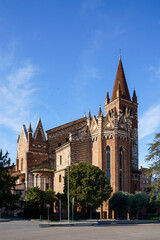 An ancient church building made of red brick with white elements in the city of Verona, Italy The sky is blue, sunny with light clouds.