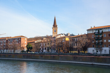 Fototapeta premium A view of part of the city on the waterfront in Verona, Italy. The tall, pointed bell tower of the church is visible