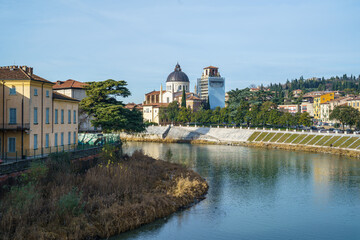 Fototapeta premium A Adige river in Verona Italy runs through a city with a large building in the background The water is calm and the sky is clear