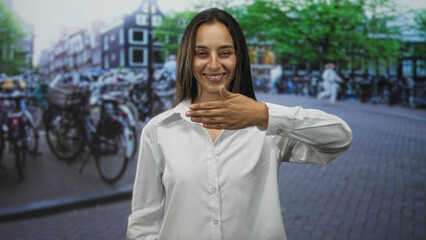 Fototapeta premium Woman covering mouth with hand and smiling on a cobblestone street with bicycles and buildings; playful secret.