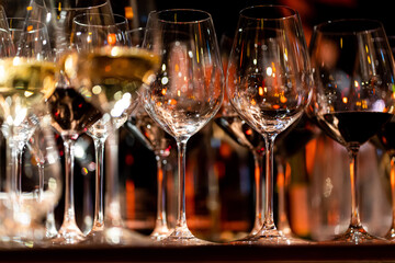 Elegant scene of wine being poured into glasses aligned in a row, showcasing the rich colors and graceful flow of the liquid, set against a dark, warm background, ideal sophisticated dining settings