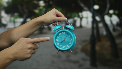 Man pointing at blue alarm clock outdoors on city street highlighting time or reminder concept.