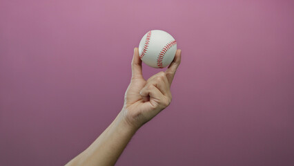 Male hand holding a baseball against a pink background, showcasing sport themes in an isolated setting.