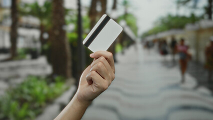 Man holding credit card on a vibrant city street, against a blurred urban background, emphasizing finance, payment, and lifestyle outdoors with modern technology interaction.