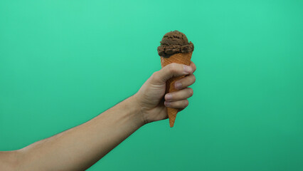 Man holding chocolate ice cream cone against a vibrant green background, showcasing a delicious snack on an isolated plain backdrop.