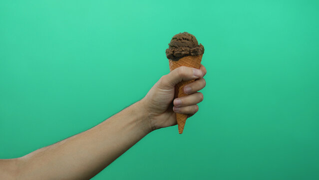 Man holding chocolate ice cream cone against a vibrant green background, showcasing a delicious snack on an isolated plain backdrop.