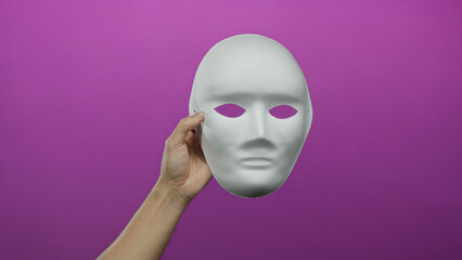 Man holding a blank white mask against a vibrant pink background, showcasing elements of anonymity and creativity isolated in a studio shot.
