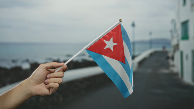Caucasian man holding cuban flag on seaside promenade, showcasing national pride in an outdoor beach setting.
