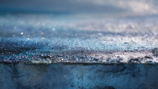 Textured blue surface sparkles with countless glistening droplets, creating an abstract, luminous scene. Soft bokeh lights in background add serene, captivating depth.