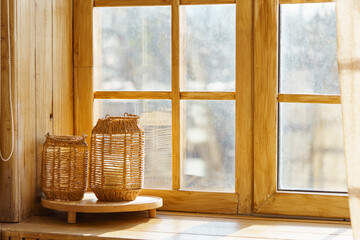 Two wicker lanterns on wooden windowsill against blurred autumn forest background. Warm natural light and cozy rustic atmosphere of fall interior design, natural materials, home decor