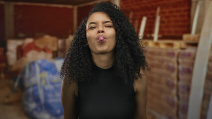 Young woman makes a mocking grin while holding hands by her head in a building interior; cheeky...