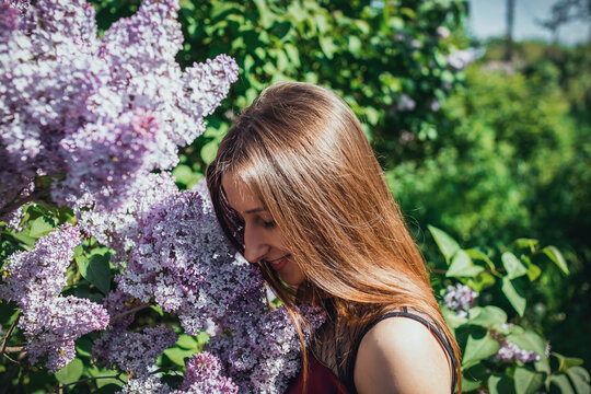 Young woman in a burgundy dress standing beside blooming lilac bush in natural spring setting