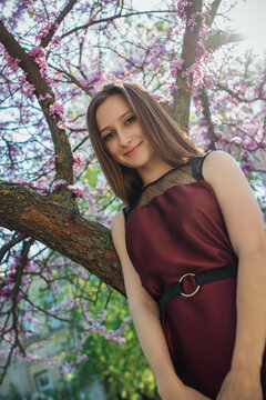 Young woman in a burgundy dress standing beside a tree with small pink blossoms