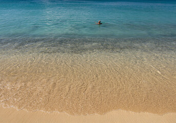 Wide image of an elderly man floating in the shallow water of a tropical beach