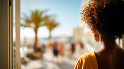 Defocused wide shot of the balcony view with the faceless woman in the foreground, standing in the open doorway, warm vacation ambiance, with copy space