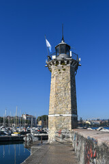 Fototapeta premium Stone lighthouse in Desenzano del Garda overlooking the marina, with boats, clear blue sky, and waterfront scenery on a sunny day.