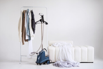 A light autumn capsule wardrobe on a rail hanger in a white room with a modern ottoman. Mockup with copy space.