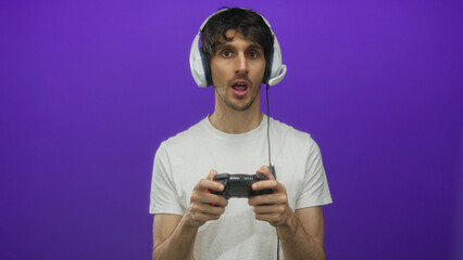 Man wearing headphones holding game controller and pressing buttons in purple studio setting; concentration.