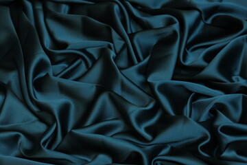 Close-up of soft, flowing teal blue Charmeuse satin texture. Ideal luxurious background for...