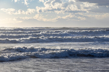 Powerful sunlit waves rolling toward the shore during stormy weather, capturing dynamic motion and bright sea spray. Mediterranean coast, Side, Turkey.