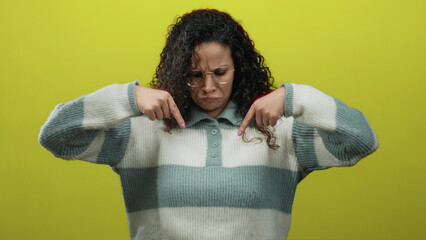 Woman gesturing with glasses and curly hair pointing downward against a bold yellow background with...