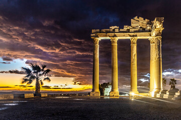 Fototapeta premium Dramatically lit Temple of Apollo at night after sunset, with Corinthian columns illuminated against a dark sky with golden sunset streak. A majestic historical site in Side, Turkey, Mediterranean.