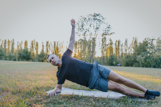 Man balancing in side plank variation on yoga mat during outdoor session - Powered by Adobe