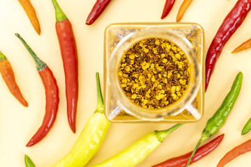 Top view of crushed red chili flakes in a glass jar with fresh colorful red, green, yellow, and orange chili peppers scattered