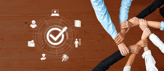 A diverse team of individuals collaborates around a wooden table, showcasing hands joined together with graphic icons symbolizing success and verification in a professional setting. Trope