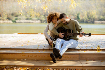 Couple enjoying music by the lake during a golden autumn afternoon with leaves falling