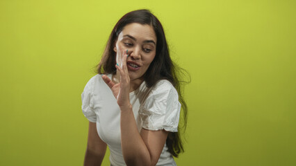Woman whispering with hand to mouth in lime green studio, smiling with closed eyes; playful amusement.