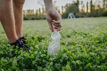 Man lifting discarded plastic bottle off grass in open air park for recycling