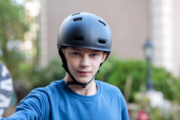Close-up portrait of a confident young teenage boy wearing a sleek black safety helmet, looking directly at the camera outdoors