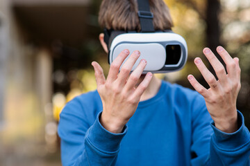 Close-up of a young teenage boy's hands gesturing and interacting with an invisible digital environment while wearing a virtual reality headset outdoors