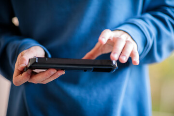 Close-up of a young person's hands holding a smartphone horizontally and typing or interacting with the screen, wearing a blue sweater