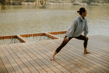 Korean woman practicing yoga on a peaceful lakeside deck during a sunny afternoon