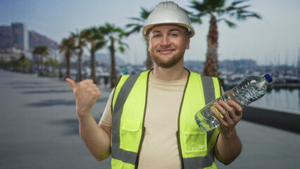 Man engineer in hardhat and high visibility vest holding a water bottle and giving thumbs up on...
