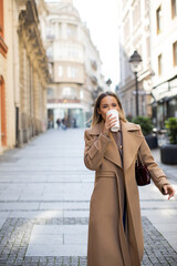 Woman enjoying a coffee while strolling through a city street on a sunny day