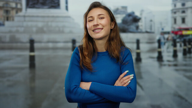 Woman smiling and crossing arms in a vibrant city street with historic architecture and iconic structures suggests a positive urban experience outdoors.