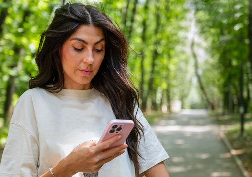Beautiful Brunette Woman using her phone in the summer park