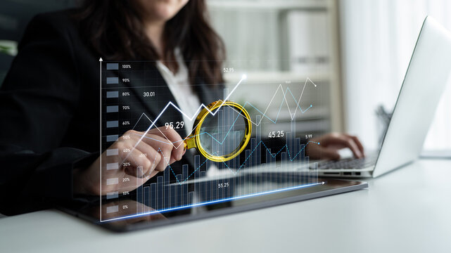 A professional businesswoman uses a magnifying glass to analyze stock market data on a laptop, surrounded by financial charts in a modern office setting. Scalp - Powered by Adobe
