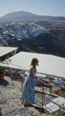 Obraz premium Woman with bare back holding railing looks toward santorini town building viewpoint; serenity travel exploration.